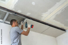 Construction worker assemble a suspended ceiling with drywall and fixing the drywall to the ceiling metal frame with screwdriver.